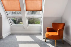 Two adjacent skylight windows in an alcove dressed in russett duette blinds partially lowered, a russett low chair sits next to them on a pale grey carpet, with walls in grey and white.
