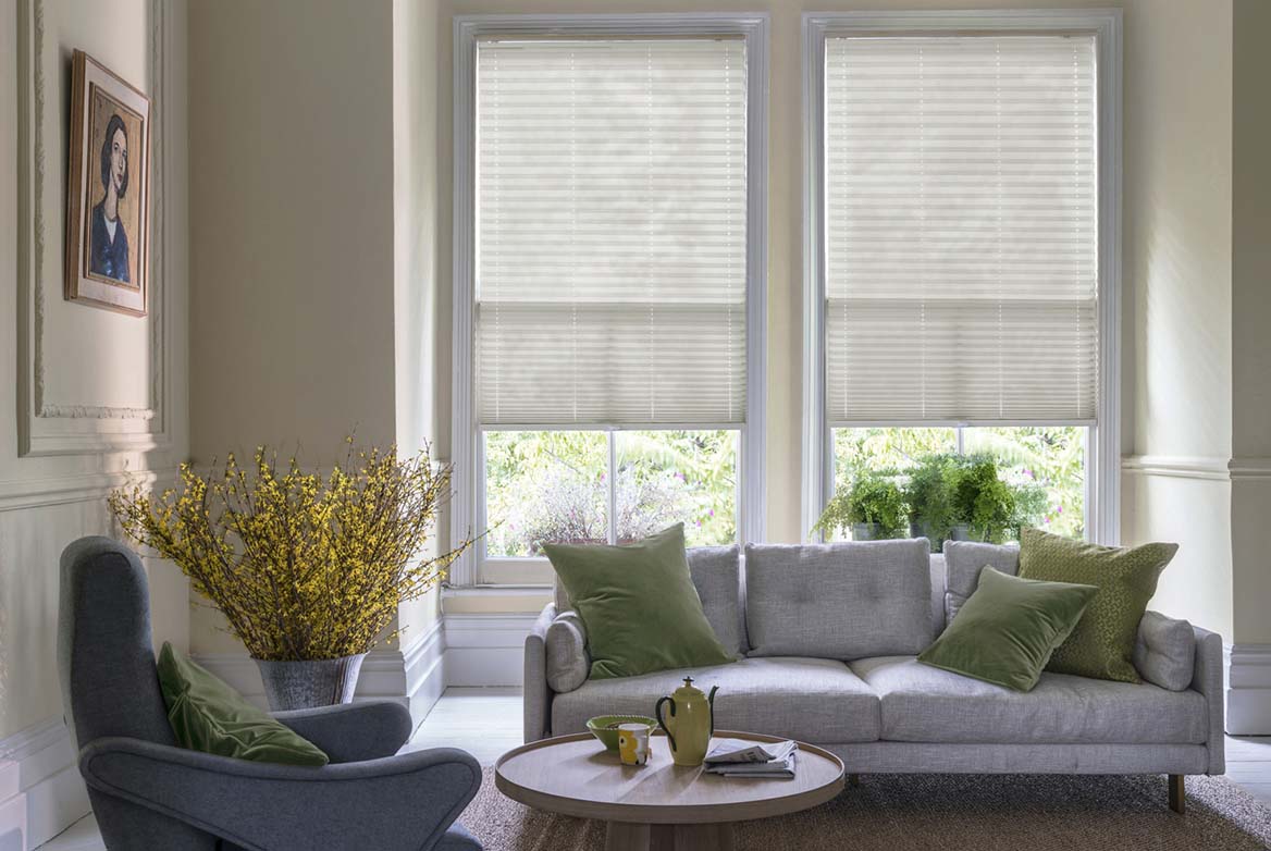 ivory Lumina Sheer Cotton White Pleated blind are fitted to a series of windows in a kitchen decorated with marble counter tops, white walls and drawers. The Pleated blinds are decorated in a plain style.