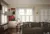 Lounge with wood floor, chocolate brown leather sofa, abstract art on walls and three sets of windows on wall to rear and left, all dressed in white tier on tier shutters, with two sets top halves open.