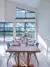 Dining area with contemporary wooden table and chairs set in front of two large windows beneath a mezzanine shaped window dressed in blue duette blinds.