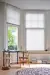 White coloured blinds fitted to bay shaped windows in a spacious study room with a desk, chair, footstool and circular rug 