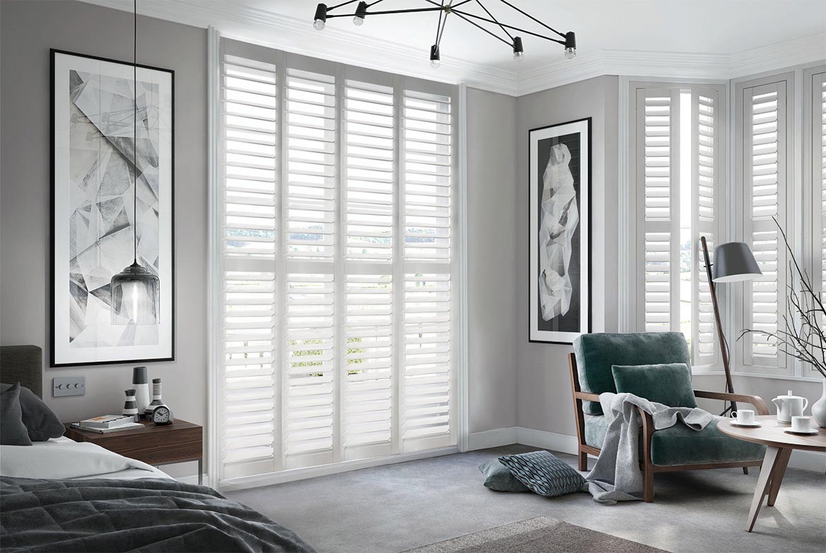 On a series of tall windows Chalk Dust Shutters have been fitted. The White colour suits the bedroom which is decorated in grey and wooden tones.
