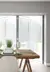 Dining room in pale grey with pale wood floor, wooden trestle-style table with white contemporary chairs, table set with white crockery and bifold doors dressed with white blinds within frame, doors partially open.