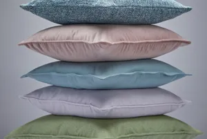 Set of cusions stacked on top of each other, olive green velvet, pale lilac, aquamarine velvet, salmon and marine blue textured.