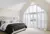 Bedroom with pale pink walls, bed wth quilted headboard dressed in white and grey bedding, gable end window and doors dressed in white shutters, doors open.