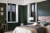 Bedroom with dark walls, bed with bedding in tones of brown and two windows on adjacent walls dressed in black tier on tier shutters with solid to lower half. 