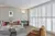  Grey ounge with full wall of white tracked shutters floor to ceiling louvres open, grey sofa terracotta cushions background, upholstered gold velvet chair foreground, a glass circular coffe table in between.