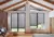 Room with brown wall and bench seating with cushions to left, wooden floor and gable end windows and doors dressed in charcoal duette blinds.