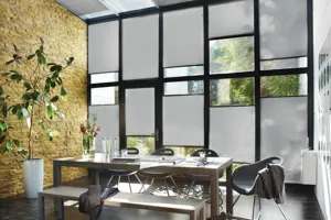 Dining room with glass walls and roof, dressed in grey Duette blinds at varying heights, dining table, chairs and benches with grey accessories