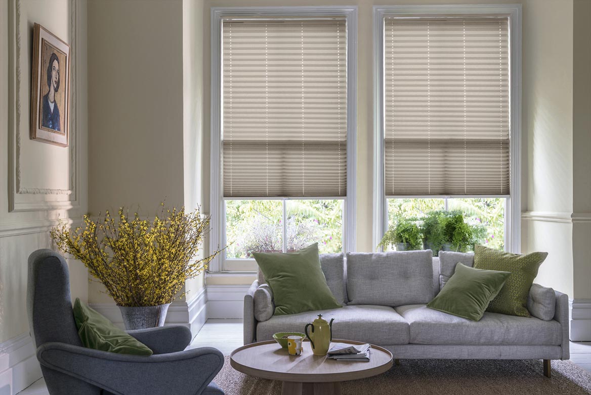 Decorated in a plain style Solartex Crush Cappuccino Crush natural Pleated blinds are fitted to windows in a kitchen with marble counter tops and cream coloured fixtures.