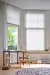 Grey coloured duette blinds fitted to bay shaped windows in a study with white walls, black desk and a chair