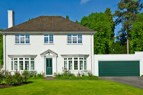 Large white house with bay windows, green door and attached garage in matching white with green door.