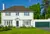 Large white house with bay windows, green door and attached garage in matching white with green door.