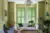 Living room with pale yellow-green walls, sofa and chairs with two tall windows in the background, dressed in mid-green shutters.