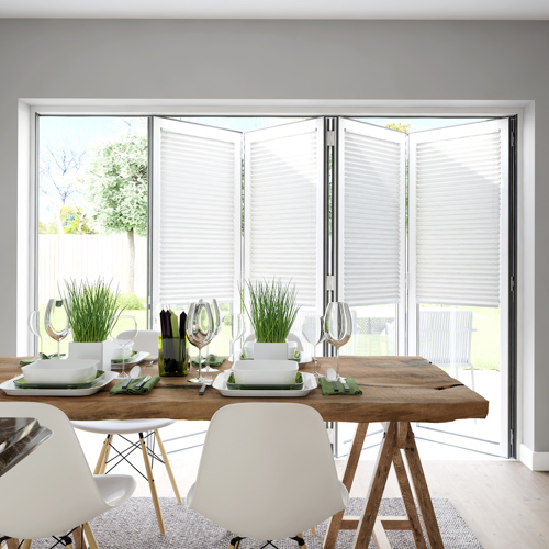 Dining room in pale grey with pale wood floor, wooden trestle-style table with white contemporary chairs, table set with white crockery and bifold doors dressed with white blinds within frame, doors partially open.