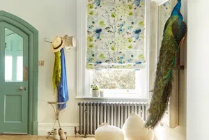 Hallway with tiled floor, coat stand with panama hat,cobalt blue and green scarves, window with Roman blind in cream with green and cobalt abstract flower pattern, reflected in mirror to right, faux peacock on shelf.