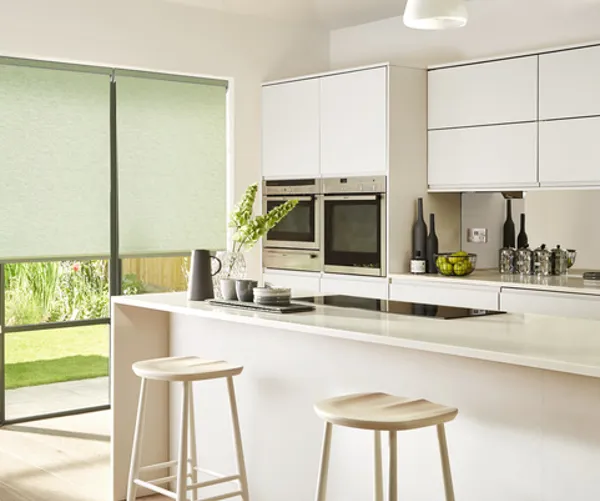 Kitchen in white with touches of green and bifold doors dressed in pale green roller blinds.
