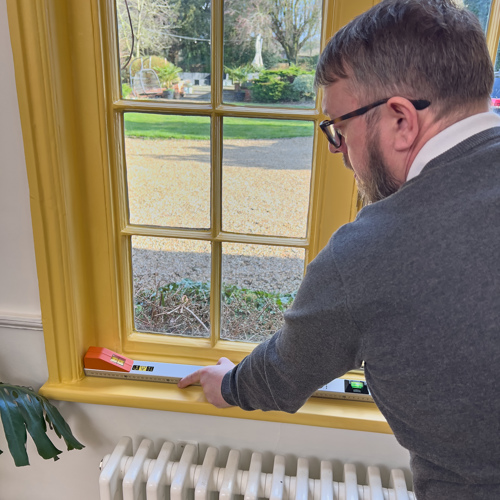 Man holiding a large spirit level and measuring tool on a window sill.