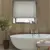 Bathroom with deep recessed window dressed in pale grey-beige roller blind, walls with wood panelling, roll top bath with central mixer taps, small bay tree in pot to left.