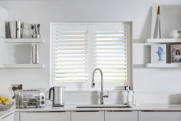 closed white vinyl shutters in kitchen window behind sink, toaster and kettle