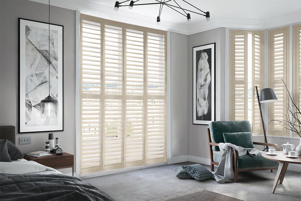 On a series of tall windows White Hart Shutters have been fitted. The Natural, White colour matches the style of the bedroom which is decorated in grey and wooden tones.