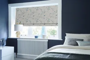 Navy blue bedroom, bed with white and blue bedding to right, large window dressed in roman blind with white background and watercolour effect blue flowers.