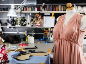 Sewing room with shelves of ribbons, mannequin with a salmon dress, threads and sewing paraphenalia on table.