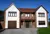 Large contemporary two-tone house with apex windows, integral garage with light brown garage door matching front door.