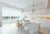 Open-plan white kitchen with trio of window and doors dressed in white roller blind with marble island with white chairs and modern pendant light.