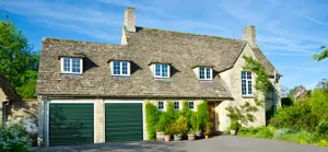Large traditional pale stone house with wide driveway and two green garage doors.