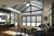 Open plan lounge diner with gable end and roof lantern windows and doors dressed in pale grey duette blinds, parquet floor, chocolate brown sofas on right, dining table and chairs on left with a geometric white and dark grey patterned rug in the middle.