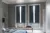 A pair of blue solid shutters fitted to tall rectangular shaped windows in a bedroom decorated with grey walls, bed and wooden breakfast table