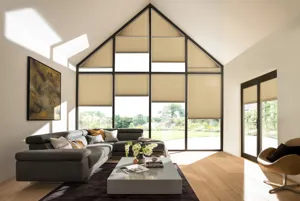 Gable end windows and doors in living room with buttermilk walls, brown sofa, grey low table, wood floor, French doors on right hand wall, all windows and doors dressed in pale caramel Duette blinds at varying heights.)