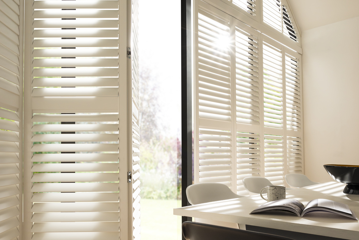 Dining room with gable end windows and doors, dressed in cream shutters partially folded back to reveal the open door.