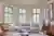 Lounge with curved bay windows dressed in pale Seaglass-coloured shutters, wooden chair on left upholstered in deep peach, pale blue shaped contemporary sofa in middle, wooden sideboard on right.