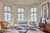 Lounge with curved bay windows dressed in pale Seaglass-coloured shutters, wooden chair on left upholstered in deep peach, pale blue shaped contemporary sofa in middle, wooden sideboard on right.