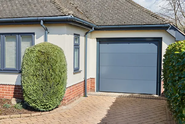 Corner shot of single storey house in white with anthracite grey integral garage door matching guttering and window frames and block paved driveway.