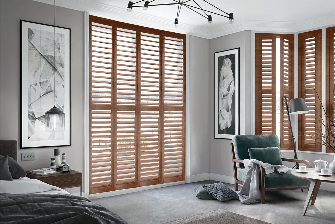 On a series of tall windows Bronzed Pecan Shutters have been fitted. The Natural, Brown colour matches the style of the bedroom which is decorated in grey and wooden tones.