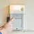 A finger presses the down button of a garage door electric wall control with a light on it and a couple of buttons.