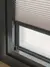 Close up of the bottom of a dark brown sliding door frame dressed with an ivory pleated blind lowered just short of the frame.