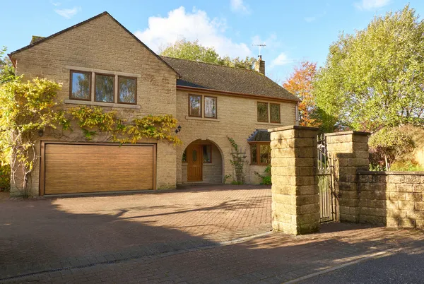 Large Yorkshire-style stone house and drive with integral garage door in mid brown matching front door, with climbing plant above garage.