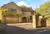 Large Yorkshire-style stone house and drive with integral garage door in mid brown matching front door, with climbing plant above garage.