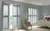 Pale blue bedroom with Queen Anne style bed ad chair and two sets of doors and windows dressed in pale blue shutters, one set partially open.