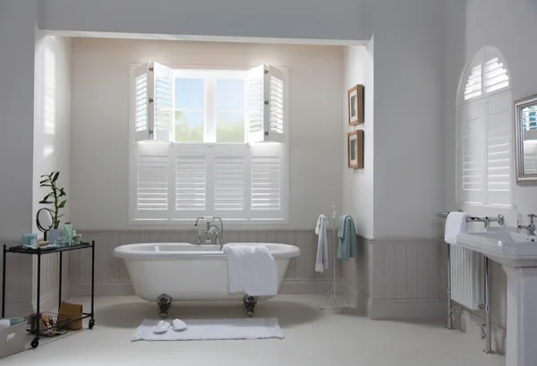 tier on tier white vinyl shutters with top half open in bathroom window behind white bathtub