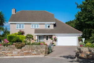 60s-style property in floral setting with dormer integral garage with white sectional garage door and matching front door.