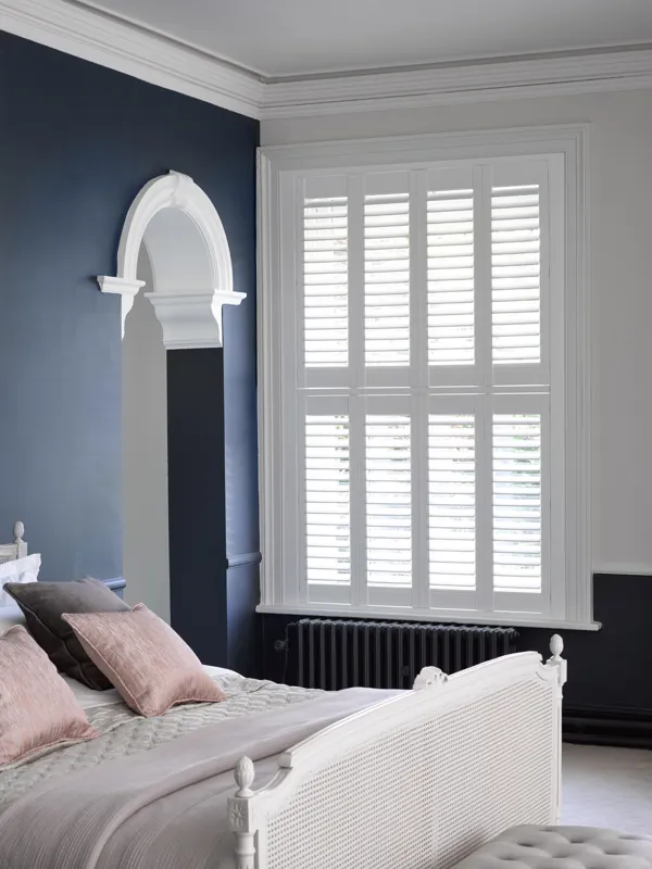 white shutters in navy blue living room with arched doorway and white bed
