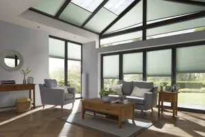 A living room with sofa and chairs in grey and gable end and sloped ceiling dressed in soft green duette blinds.