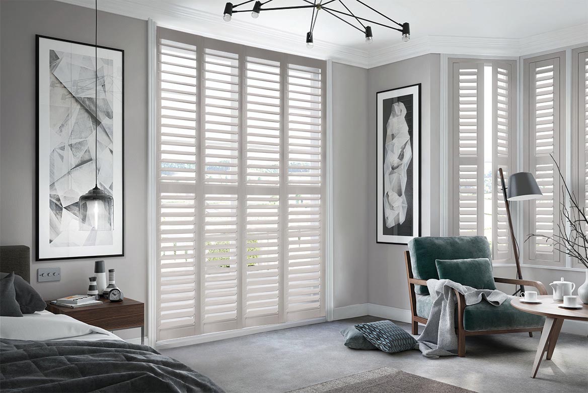 On a series of tall windows Pebbled Lane Shutters have been fitted. The Grey colour suits the bedroom which is decorated in grey and wooden tones.