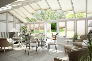 Rectangular conservatory with tiled floor, wingback sofa and chairs, cast iron table and chairs and pitched roof windows, doors and side windows all dressed in cream duette blinds at varying heights.