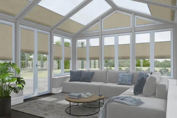 White conservatory with windows and doors dressed in creamy-beige duette blinds at varying heights with some roof blinds open, wooden floor, neutral l-shaped sofa, round coffee table on a cream rug.